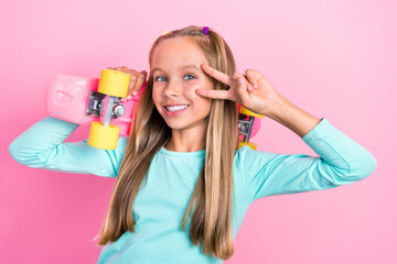 Poster - Portrait of positive cute girl hold skateboard show v-sign near eye toothy smile isolated on pink color background