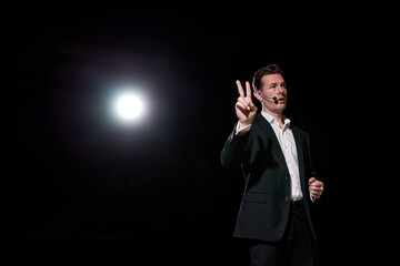 Man speaking through microphone in dark conference hall, on stage, performance. Person in suit says about marketing and management for successful sales to audience. Professional ideas