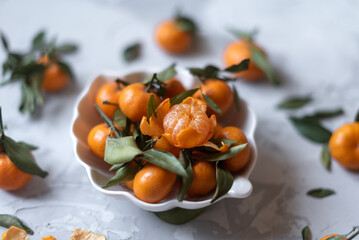 Fresh mandarin orange fruits or tangerines with leaves on a gray background or table in a white plate