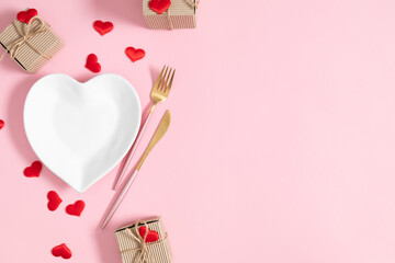 Wall Mural - Valentine's Day concept. Heart shaped white plate and cutlery fork and knife, heart shaped confetti gift box on isolated pastel pink background. Flat lay, top view, copy space