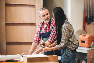 Wall Mural - Small business furniture owner and professional architect interior designer working in carpenter workshop with blueprint and tablet discussing about home furnishing design project.