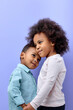© alfa27 - two pretty kid friends hugging holding hands together isolated over purple pastel color background, adorable kid boy and girl in casual wear posing happily. portrait. children