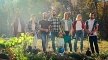 Portrait Of Caucasian Team Of Eco Activists, Men And Women Standing Together In Park With Seedlings Of Trees And Small Kid And Posing To Camera. Outdoors. Males, Females And Child Planting Tree.