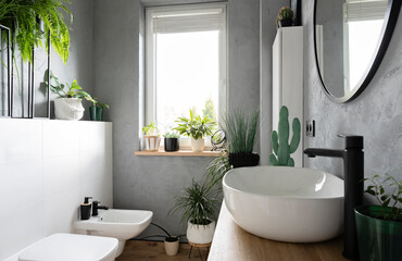 Wall Mural - Stylish bathroom with window and green plants. Ceramic wash basin with tap, toilet, bidet and round mirror on the grey wall. New design in modern apartment.