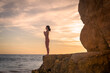 © Rob Wilkinson - Woman standing on rocks by the sea practicing yoga at sunrise or setset.