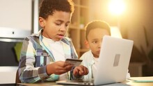 Two Cute Little African American Boys Brothers Paying With Credit Card On Laptop Computer At Home Happy Young Kids Customers Doing Payments Online Shopping Buy Toys In Internet Store
