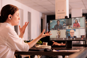 Wall Mural - Woman attending online corporate meeting on computer, talking with remote colleagues, coworkers teleconference communication. Business plan discussion on videoconference in coworking space at night