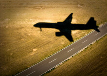The Shadow Of An Airliner Crosses An Empty Road As It Approaches The Runway.