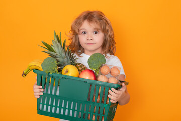 Wall Mural - Food store. Child grocery cart, isolated studio yellow background with copy space. Little shopper. Kid holding shopping basket. Fresh organic, vegetables and fruits in grocery food store