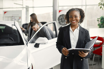 Black saleswoman standing at auto showroom and looking at camera