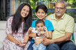 © GAJENDRRA BHATI  - Portrait of Happy indian grand parents sitting with their grand children at home. Asian senior and young couple with kids looking at camera.