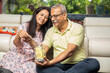 © GAJENDRRA BHATI  - Happy mature senior Indian couple putting money in jar full of rupee notes in hand while sitting at home. Savings and banking concept