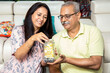 © GAJENDRRA BHATI  - Happy mature senior Indian couple putting money in jar full of rupee notes in hand while sitting at home. Savings and banking concept