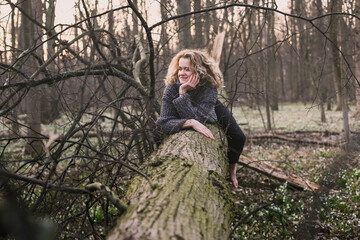 Wall Mural - Curly haired lady resting on tree trunk scenic photography. Picture of person with wild wood on background. High quality wallpaper. Photo concept for ads, travel blog, magazine, article