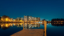 Night View On Tysiaclecie Estate In Katowice, Silesia, Poland. Lightened Residential Buildings With Surrounding Trees At Dusk Seen Through The Lake. Little, Wooden Jetty In The Foreground.