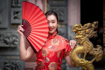 Portrait beautiful Asian woman wearing traditional cheongsam qipao dress nice smile holding red fan in Chinese festival concept.