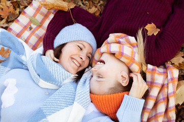 Wall Mural - Top view of laughing family of young woman, teenage girl hugging, lying head-to-head on yellow fallen leaves in forest.