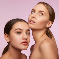 Youth, tenderness. Portrait of two young, beautiful girls with well-kept skin isolated over pink studio background. Concept of skincare, cosmetology, natural beauty