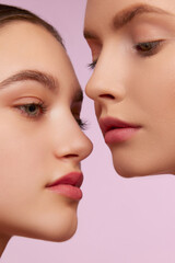 Portrait of two young, beautiful blonde and brunette girls with well-kept skin isolated over pink studio background. Concept of skincare, cosmetology, natural beauty