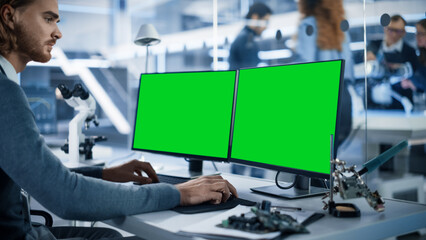 Wall Mural - Software Developer Working on Computer with Green Screen Mock Up Display. Scientific Lab, Engineering Research Center with Specialists Working on Mobile Robot Development in the Background.