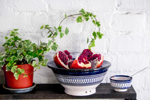 Close-up Of Pomegranate In Plate On Bowl By Potted Plant On Table Against Brick Wall