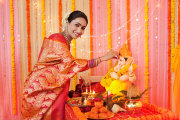 Portrait of an Indian woman putting tilak on Lord Ganpati's idol - Festival celebration. Stock image of a woman in saree celebrating the festival with happiness and joy - putting tilak on Lord Gane...