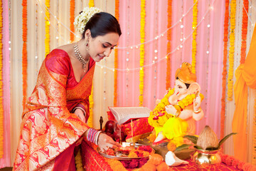 Portrait of a young happy woman doing Ganesh puja/pooja on Ganesh Chaturthi: Indian festival culture. Indian woman wearing silk saree is doing Ganesh puja / pooja and placing the dhoop in thali - H...