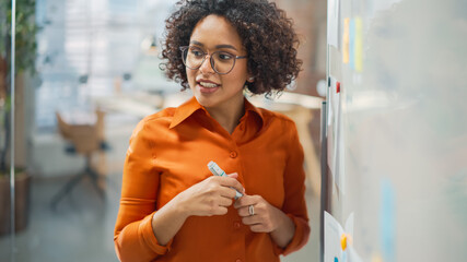 Poster - Portrait of a Beautiful Black Woman in Smart Casual Clothes Doing a Presentation in a Meeting Room for her Colleagues. Female Team Lead Explaining Data and Statistics Using a Whiteboard and a Marker