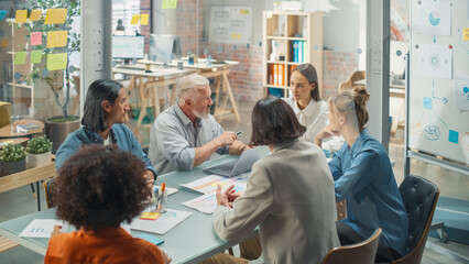 In the Meeting Room Team of Entrepreneurs and Specialists sitting at the Conference Table Have Discussions about Statistics and Charts, Solve Problems, Led by Senior Lead. They are Using Laptop