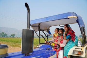 Happy Indian farmer family sitting on tractor at agriculture field.