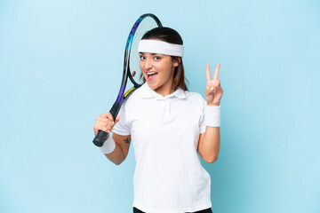 Wall Mural - Young tennis player woman isolated on blue background smiling and showing victory sign