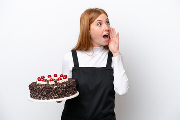 Wall Mural - Young redhead woman holding birthday cake isolated on white background shouting with mouth wide open to the side