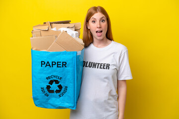 Wall Mural - Young redhead woman holding a recycling bag full of paper to recycle isolated on yellow background with surprise facial expression