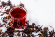 Hibiscus tea in a glass mug and scattered hibiscus on white background, perspective view. Available copy space.Herbal tea for healthy life.