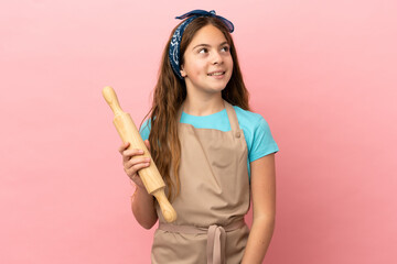 Poster - Little caucasian girl holding a rolling pin isolated on pink background thinking an idea while looking up