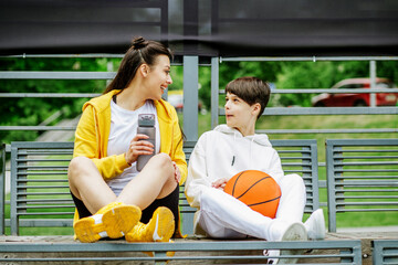 Wall Mural - Young brother and sister are talking and having fun on sports ground during break. Family concept.