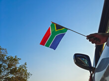 Boy Waving South Africa Flag Against The Blue Sky From The Car Window Close-up Shot. Man Hand Holding South African Flag
