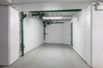 An empty parking garage spot with white walls, green pipes, and concrete floor.