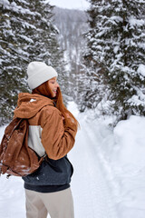 Wall Mural - Rear Ciew On Red-haired Female In Stylish Warm Coat With Backpack Walking In Wonderful Winter Forest Alone, Outdoors. Healthy Lifestyle, Recreation, Travel, Hiking, Happiness, Adventure Concept