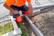 Builder in orange ho-viz protective closing placing edging pin kerb into semi-dry concrete using a string line to keep them straight during construction of the footpath