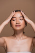 © LIGHTFIELD STUDIOS - Young asian woman in top touching forehead isolated on brown.
