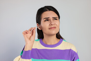 Canvas Print - Young woman cleaning ear with cotton swab on light grey background