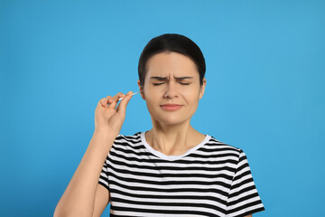 Poster - Young woman cleaning ear with cotton swab on light blue background