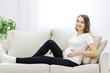 © Andrii - Pregnant woman wearing casual clothes on white sofa.