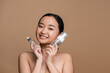 Cheerful asian model holding serum and face foam isolated on brown.