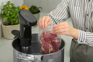 Wall Mural - Woman putting vacuum packed meat into pot in kitchen, closeup. Thermal immersion circulator for sous vide cooking