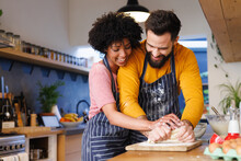 Playful Cheerful Biracial Young Couple Kneading Dough Together On Kitchen Counter