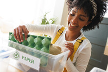 Close-up Of Smiling Biracial Young Woman Sorting Paper Garbage In Recycling Bin, Copy Space
