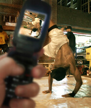 A street performer break dances, while a spectator takes a picture with his cellphone (foreground), on 2nd Ave..