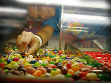 A Younger Female Worker At A Candy Shop Scoops Some Jellybeans For A Customer.